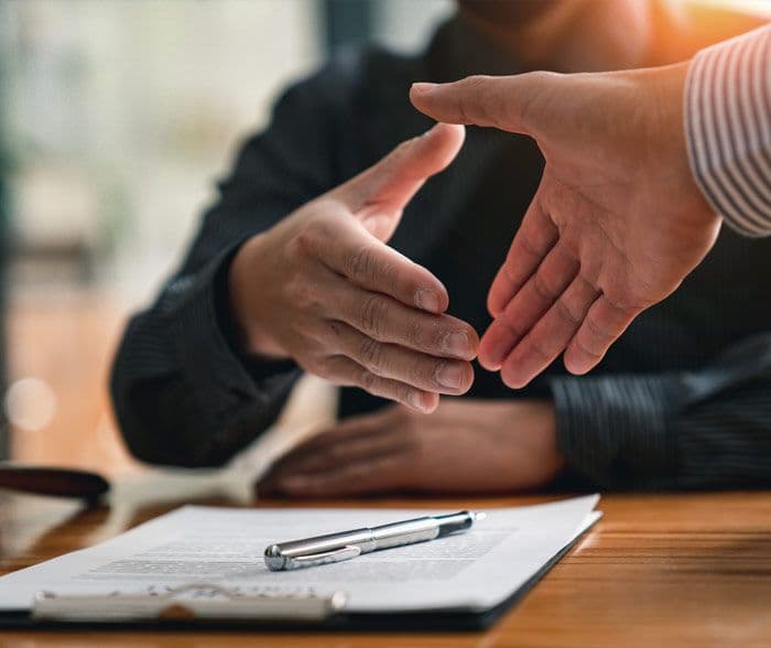 Two people about to shake hands with a pen and paper below them
